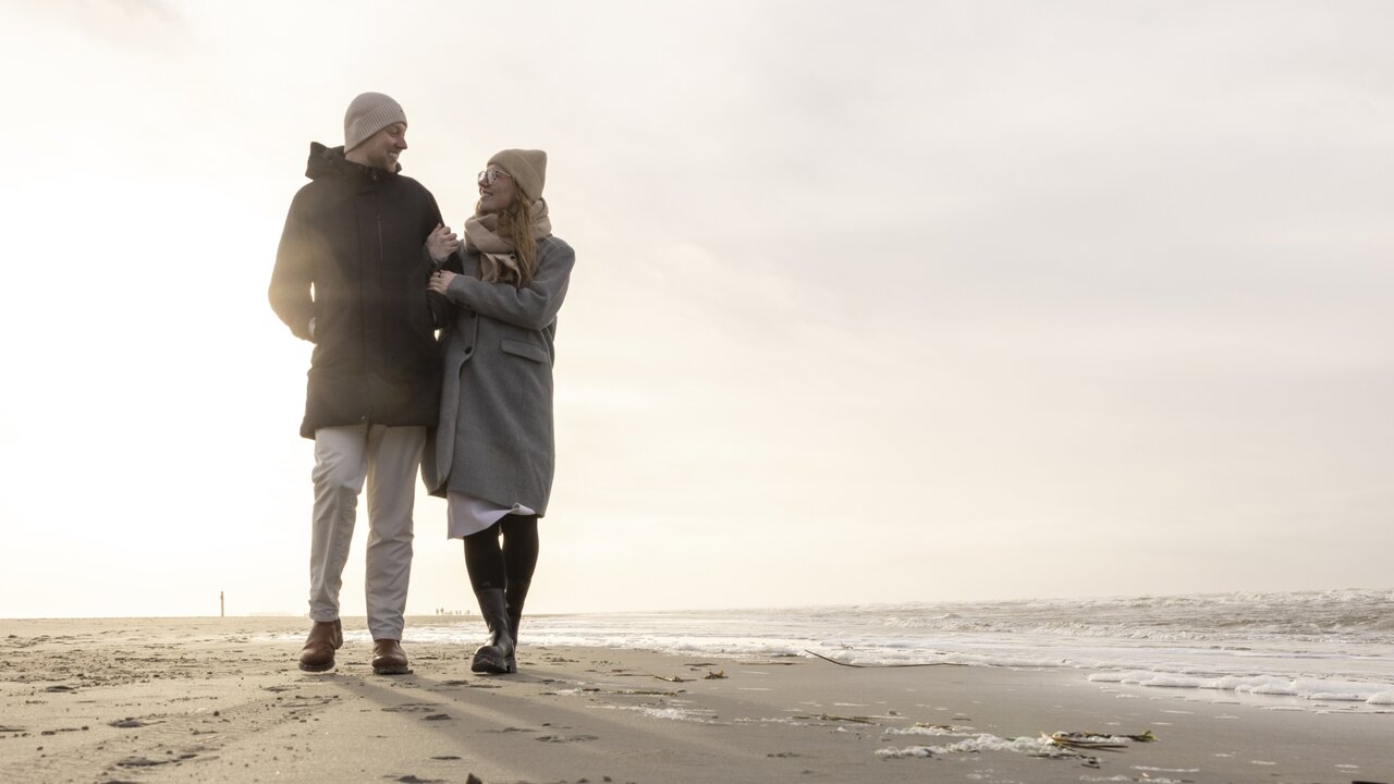 Paar in Winterkleidung am Strand, lächelnd und sich anblickend, YouTube-Video-Thumbnail
