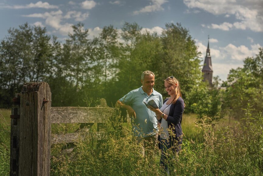 Personen vor einer Wiese mit Kirchturm im Hintergrund