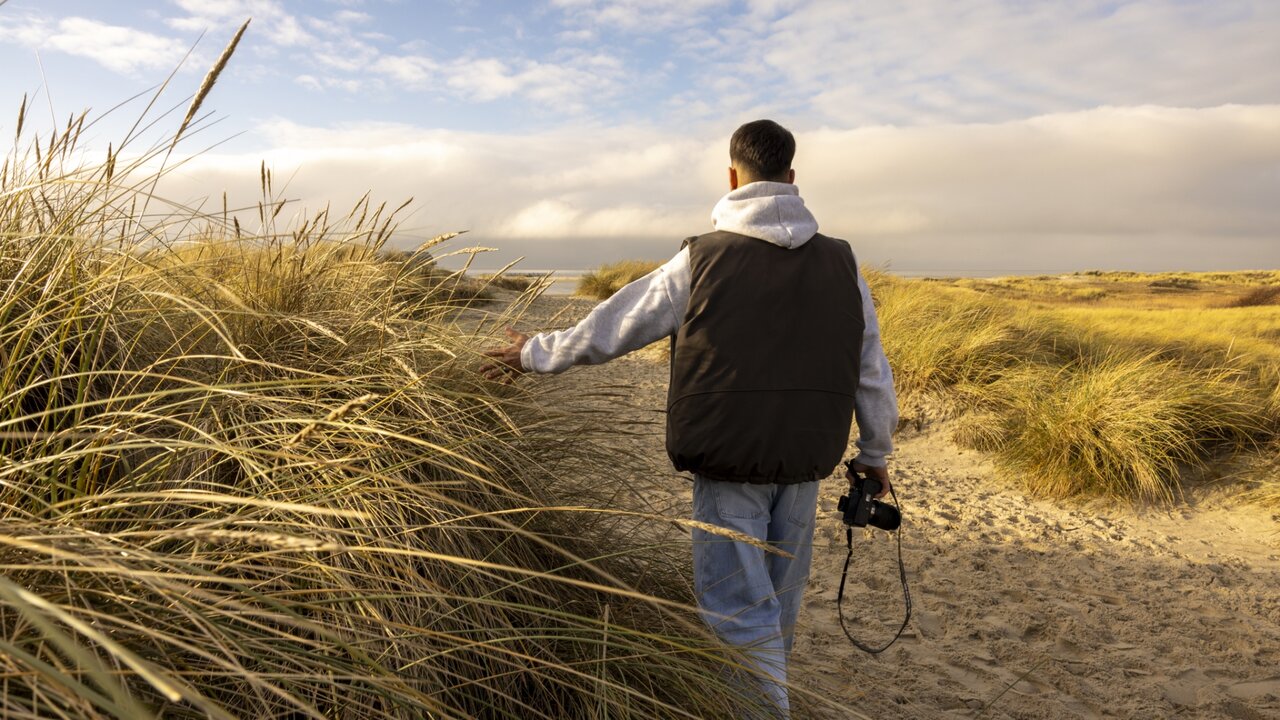 Mann mit Kamera steht am Strand und blickt aufs Meer bei bewölktem Himmel, YouTube-Video-Thumbnail