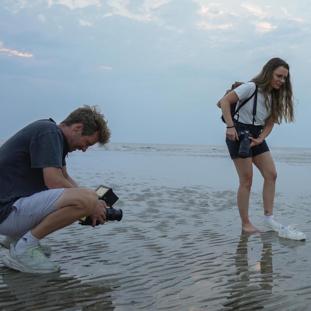 Marina steht barfuß am Strand und wird vom Kameramann gefilmt