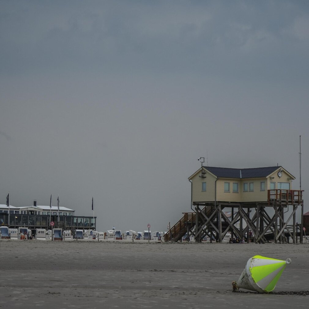 Ein Pfahlbau am Strand – im Vordergrund liegt eine Boje