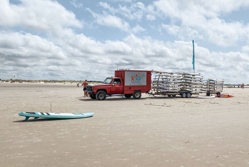 A car from the XH2O Water Sports Center with a trailer full of surfboards
