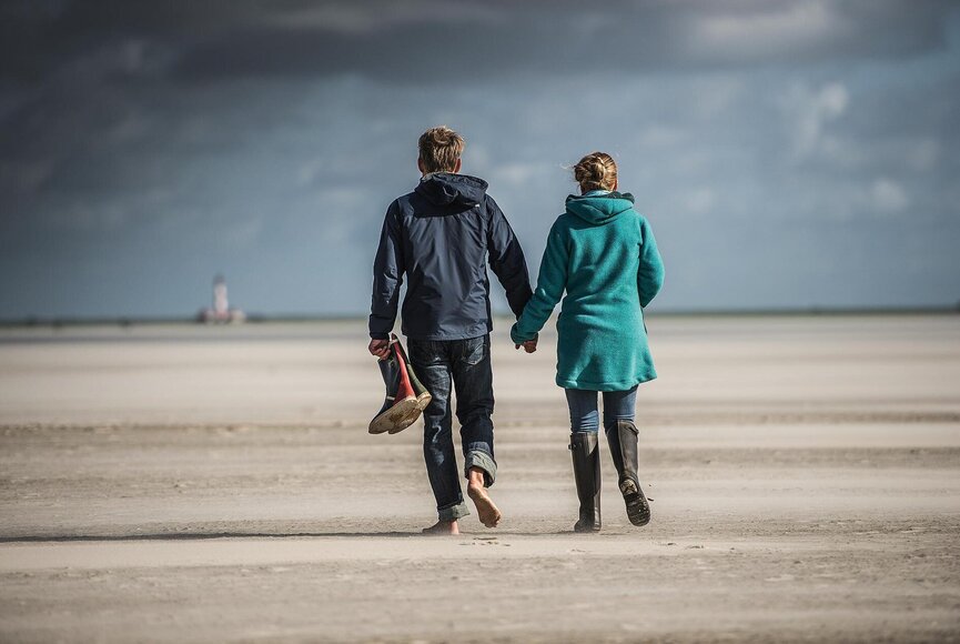 Paar beim Strandspaziergang im Herbst mit Regenjacken und Gummistiefeln