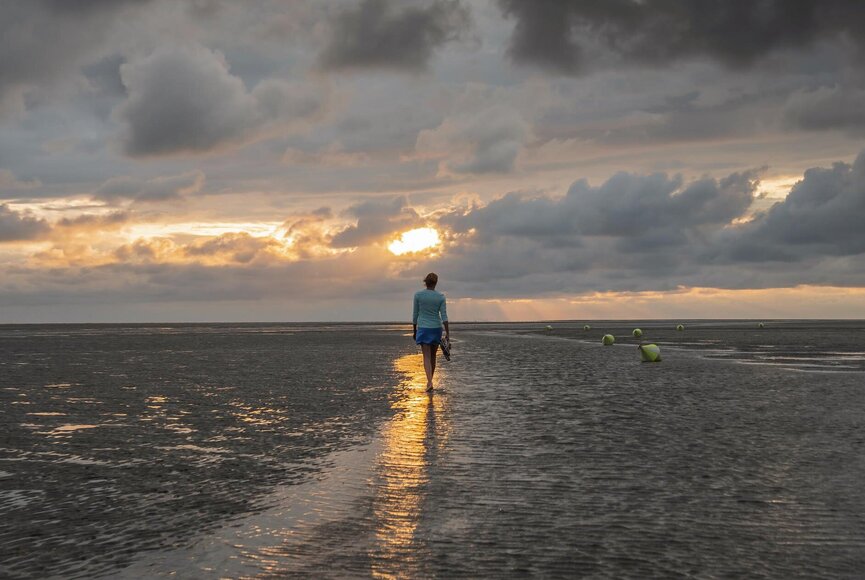 Spaziergängerin an der Wasserkante bei Sonnenuntergang