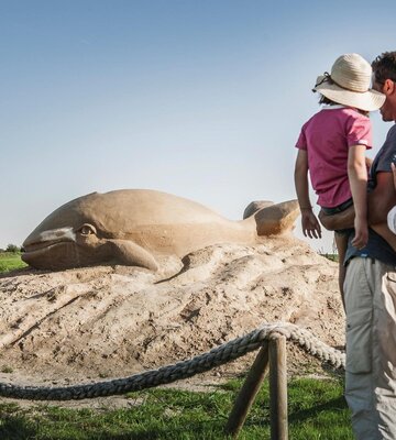 Familie steht vor Sandskulptur in Form eines Wals