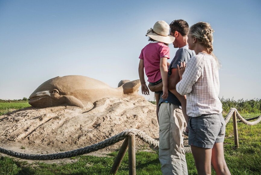 Familie vor einer Sandskulptur eines Wals