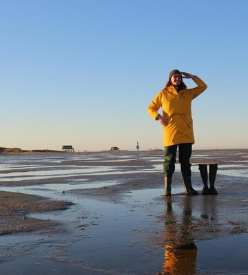 Person mit gelbem Friesennerz und Gummistiefeln am Strand