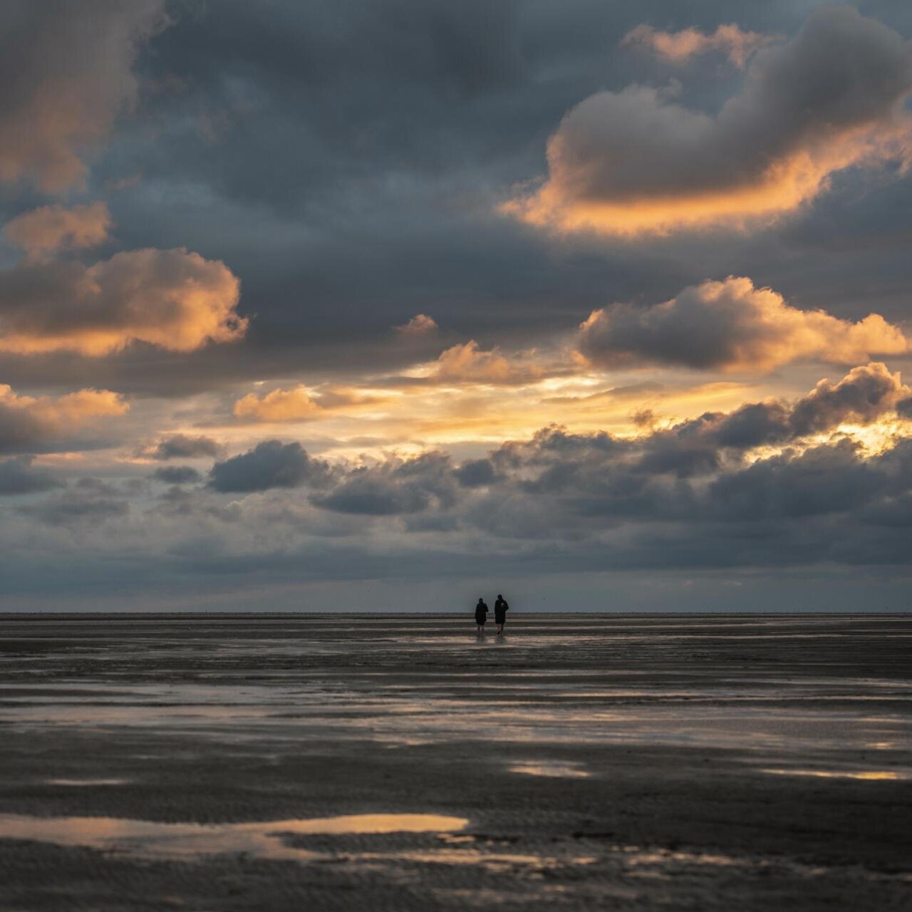 Spaziergang eines Paares bei Sonnenuntergang am Wattenmeer