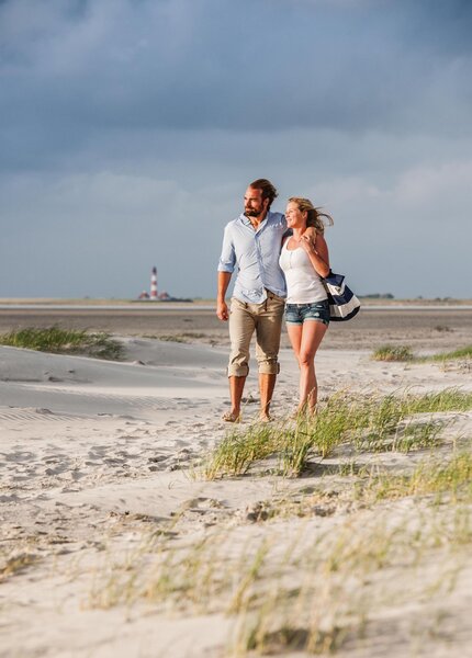 Paar beim Strandspaziergang mit Westerhever Leuchtturm im Hintergrund